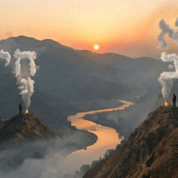 Silhouetted people by a campfire overlooking a foggy mountain valley during sunrise.